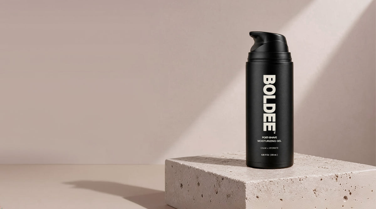 Black pump dispenser bottle of BOLDEE Post-Shave Moisturizing Gel resting upright on a porous, light-gray stone pedestal with natural light and soft shadows.